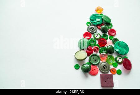 Ein Weihnachts- oder Apfelbaum aus Knöpfen in grüner, roter Farbe. Mehrfarbige Fäden mit Holzspulen. Weißer Hintergrund, Kopierbereich. Kreatives Konzept. Stockfoto