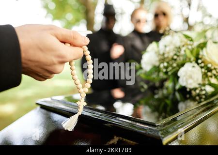 Nahaufnahme eines Mannes, der Rosenkranz hält und bei der Beerdigung betet, Kopierraum Stockfoto