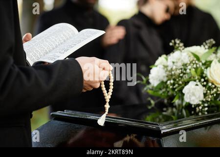 Nahaufnahme einer Person in Schwarz, die auf einer Beerdigung im Freien betet und die Bibel mit Rosenkranz hält, Kopierraum Stockfoto