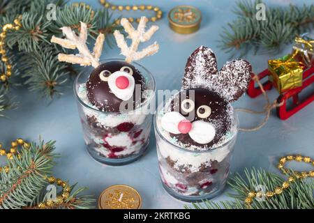 Kuchen in Gläsern in Form von süßen Kaninchen und Hirschen mit Kirschen, Schokoladenkeks und Kokosflocken auf blauem Hintergrund Stockfoto