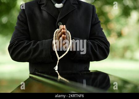 Nahaufnahme eines afroamerikanischen Priesters, der schwarz auf einer Beerdigung im Freien trägt, mit Fokus auf den Händen im Gebet Stockfoto