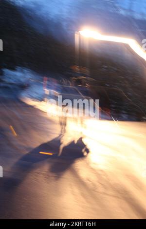 Abstraktes verschwommenes Konzept von zwei Personen, die spät nachts mit Lichtern entlang einer Straße spazieren und lange Schatten werfen. Konzept für verschwommene Welt, Schwindelgefühl Stockfoto