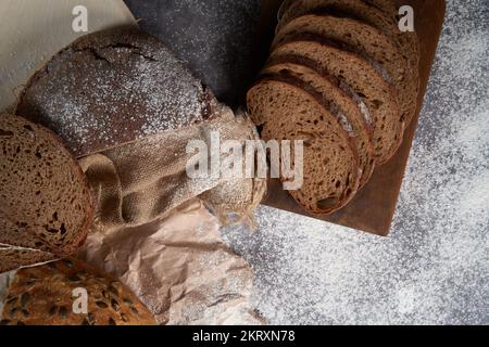 Draufsicht auf verschiedene Brotsorten, geschnitten und ganz, Mehl, zerknittertes Papier und Latte auf einem Holztisch. Flach verlegt. Stockfoto