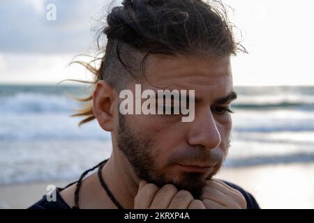 Hipster-Mann mit Händen am Kinn am Strand. Beunruhigte Einstellung. Stockfoto