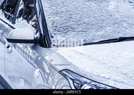 An einem Wintertag war die Windschutzscheibe eines gefrorenen Autos bedeckt und der Rückspiegel war mit Eis und Schnee bedeckt. Nahaufnahme. Stockfoto