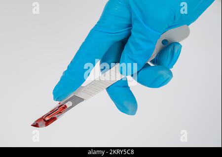 Weibliche Hand in einem Handschuh mit einem blutigen Skalpell auf weißem Hintergrund. Stockfoto