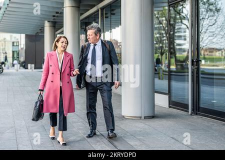 Selbstbewusste Geschäftspartner, die durch die Stadt spazieren und über die Arbeit reden, attraktiver älterer Mann mit attraktiver reifer Frau, die ins Büro geht Stockfoto