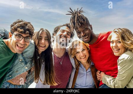 Porträt von sechs Menschen, die an sonnigen Tagen vor der Kamera lächeln, eine Gruppe von Freunden mit mehreren Rassen, die lustige Momente haben Stockfoto