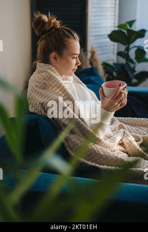 Seitenansicht einer hübschen Ingwer, die Kaffee trinkt, während sie sich zu Hause ausruht. Positive Emotionen. Ein glücklicher Lebensstil. Gemütlich Stockfoto