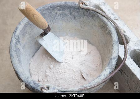 Kelle mit Holzgriff in einem Eimer mit Sand in der Nähe eines 4 Zoll großen Betonblocks Stockfoto