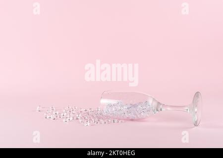 Verschüttetes Weinglas mit Diamanten auf pinkfarbenem Hintergrund. Kreatives minimales Partykonzept. Stockfoto