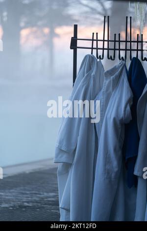Bademäntel, Handtücher hängen an einem Kleiderständer, der draußen in der Nähe des Eingangs zum beheizten Winterpool steht Stockfoto