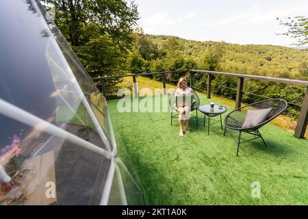 Positive Frau, die auf einem Laptop chattet und auf einen Bildschirm in der Nähe der geometrischen Struktur der Kuppel schaut Stockfoto