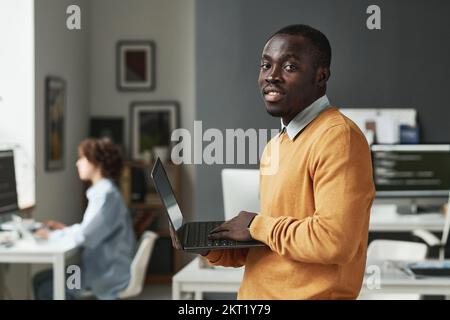 Porträt eines afroamerikanischen IT-Entwicklers, der in DER IT-Abteilung auf ein Notebook schaut Stockfoto