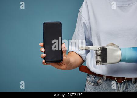 Zugeschnittenes Bild einer Frau mit bionischer Hand, die auf den Smartphone-Bildschirm zeigt Stockfoto