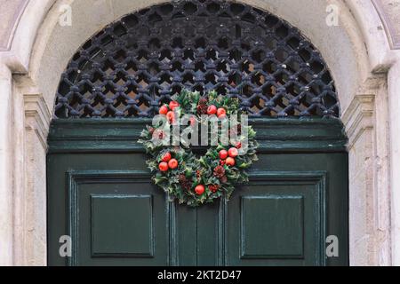 Traditioneller grüner und roter Weihnachtskranz hängt an der Eingangstür des Hauses Stockfoto