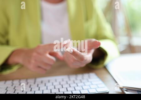 Die Frau zählt auf ihre Finger, wenn sie mit der Computertastatur am Tisch sitzt. Stockfoto