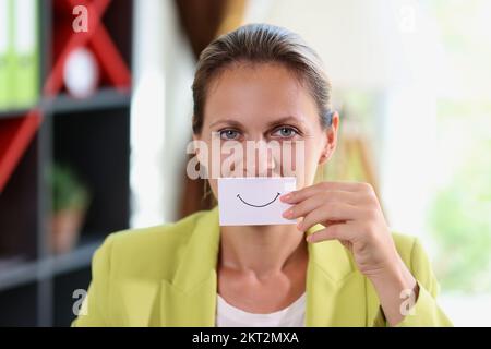 Eine Frau im Büro hält Papier mit einem fröhlichen Lächeln vor den Mund. Stockfoto
