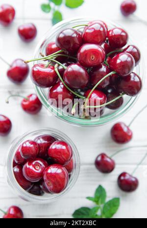 Frische rote Kirschen Früchte in Gläsern auf weißem Holzhintergrund Stockfoto