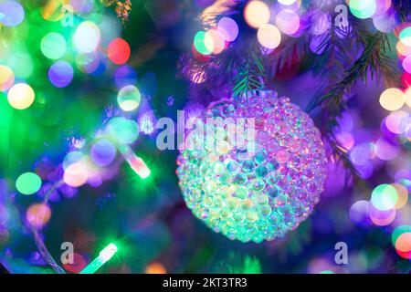 Traditionelles Weihnachtsbaumspielzeug wunderbarer Weihnachtsball mit Glasstruktur, der in einem Weihnachtsbaum mit bunten Neon-Weihnachtslichtern hängt. Weihnachten festliche Dekoration Stockfoto