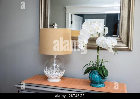 Tischdekor im vorderen Eingangsbereich mit Lampe und Orchidee, Spiegel und orangefarbenem Läufer auf einem grauen Frisiertisch Stockfoto