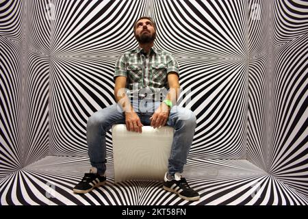 Junger Protagonist auf gelbem Stuhl und schwarz-weißer psychedelischer Hintergrund in einem modernen Raum Stockfoto