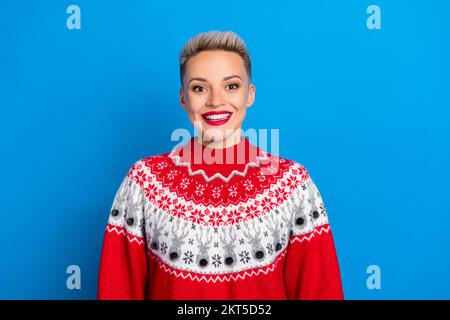 Foto eines fröhlichen, niedlichen, positiven Mädchens mit kurzer Frisur, roter Pullover, mit einem lächelnden, isolierten blauen Hintergrund Stockfoto