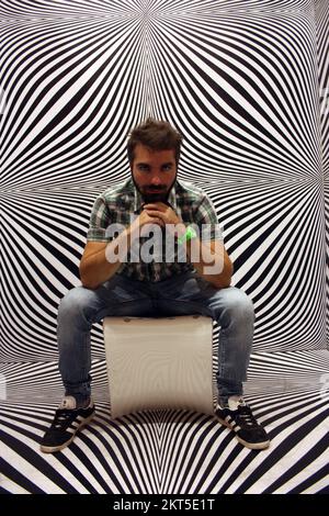 Junger Protagonist auf gelbem Stuhl und schwarz-weißer psychedelischer Hintergrund in einem modernen Raum Stockfoto