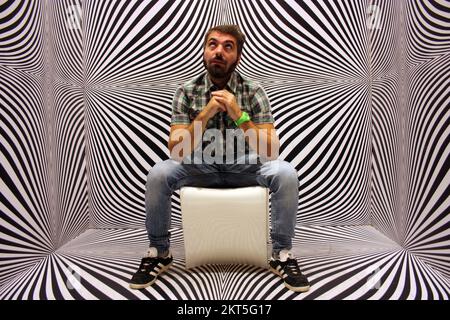 Junger Protagonist auf gelbem Stuhl und schwarz-weißer psychedelischer Hintergrund in einem modernen Raum Stockfoto