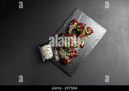 Asiatisches Essen. Hausgemachte koreanische würzige Hähnchenflügel mit Sesamsamen. Hühnerflügel. Traditionelles asiatisches Rezept. Dunkler Hintergrund. Draufsicht. Stockfoto