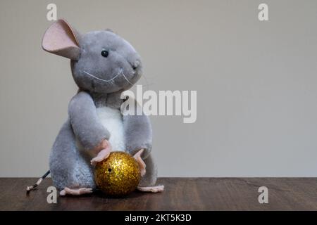 Nahaufnahme eines süßen grauen und weißen sitzenden Teddyhasen mit einer goldenen Kugel auf hellem Hintergrund Stockfoto