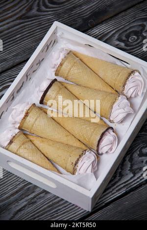 Waferkonen gefüllt mit Marshmallows. Verpackt in einem Holztablett. Hausgemachter zephyr. Auf Pinienbrettern. Von oben genommen. Stockfoto