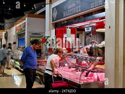 Kunden, die Fleisch in einem kleinen traditionellen Metzgerstand im Mercado del Puerto Markt auswählen Stockfoto