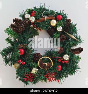 Weihnachtskranz handgefertigt aus künstlichen Fichtenzweigen, Weihnachtsdekorationen, Kiefernzapfen und getrockneten Früchten Stockfoto