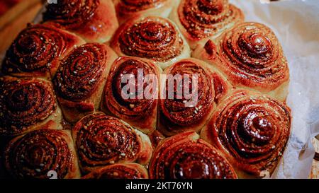 Frisch gebackene Zimtbrötchen mit Gewürzen und Kakaofüllung auf Pergamentpapier. Draufsicht. Süßes hausgemachtes Gebäck, weihnachtsgebäck. Nahaufnahme. Kanelbule - Stockfoto