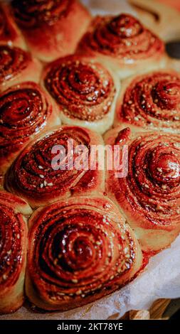 Frisch gebackene Zimtbrötchen mit Gewürzen und Kakaofüllung auf Pergamentpapier. Draufsicht. Süßes hausgemachtes Gebäck, weihnachtsgebäck. Nahaufnahme. Kanelbule - Stockfoto