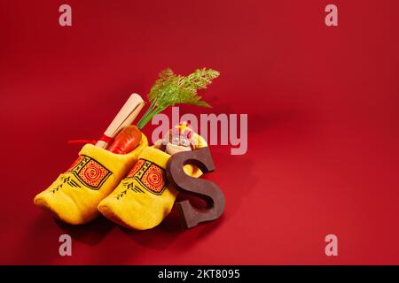 St. Nikolaus - Sinterklaas-Tag mit Schuhen, Karotten und traditionellen Süßigkeiten auf rotem Hintergrund Stockfoto