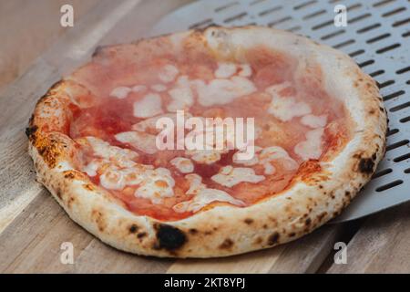 Serviert heiße Pizza Margherita mit Tomatensoße und Mozzarella mit einer Schaufel auf einem Holzbrett, mit Rauch Stockfoto