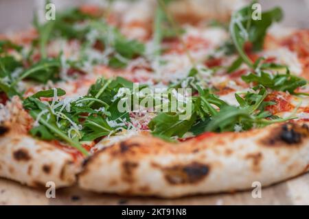 Heiße Pizza mit Tomatensauce, Mozzarella, Parmesankäse und frischen Raketenblättern auf einem Holzbrett, Nahaufnahme Stockfoto