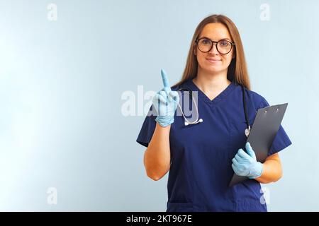 Frau Doktor mit Stethoskop und Klemmbrett, die mit dem Finger nach oben zeigt Stockfoto