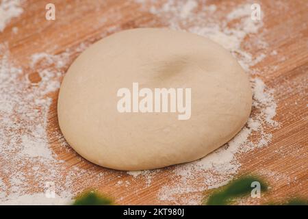 Teig für Pizza auf einem Holzbrett mit weißem Mehl und Zutaten, fertig für die Zubereitung, Nahaufnahme Stockfoto