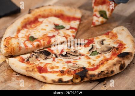 Ein Stück heiße Pizza mit Tomatensauce, Mozzarella, Basilikum und Pilzen auf einem Holzbrett mit Rauch essen Stockfoto