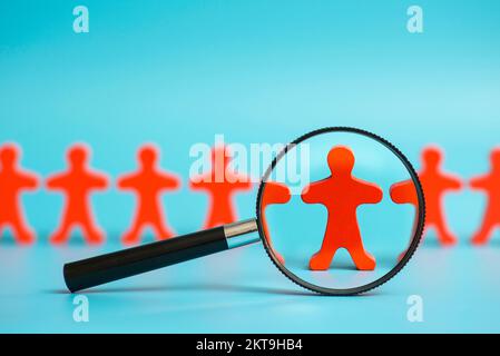 Sehen Sie durch eine Lupe auf eine hölzerne rote Person zwischen anderen Personen Stockfoto