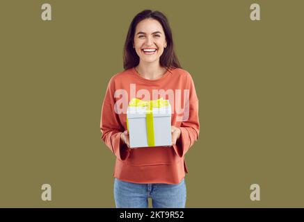 Eine fröhliche, brünette Frau in rotem Sweatshirt hält ein Geschenk in den Händen auf Khaki-Hintergrund. Stockfoto