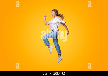 Durchgehendes Profilfoto einer lustigen jungen Frau, die schnell im Angebot ist und eine Jacke, Jeans und Turnschuhe auf gelbem Hintergrund trägt. Gelb Stockfoto