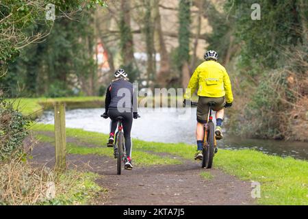 Rückansicht von zwei Radfahrern (Mann und Frau) auf Fahrrädern, die zusammen auf dem Abschleppweg entlang des Kanals fahren, Großbritannien. Stockfoto