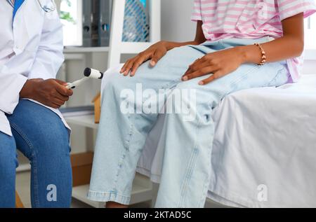 Neurologe prüft Knie- und Sehnenreflexe bei jungen Mädchen mit Hilfe eines neurologischen Schlaghammers. Stockfoto