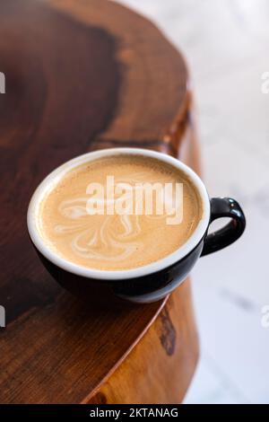 Frisch servierte Tasse Cappuccino mit Latte Art auf einem Holztisch in einem Café. Stockfoto
