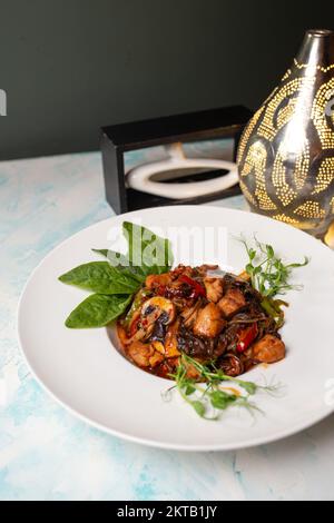 udon mit Pilzen und Huhn, Gemüse und Spinat auf einem Teller in einem Café. Stockfoto
