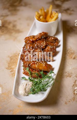 Flügel in Sesamsauce und pommes auf einem weißen Teller. Stockfoto